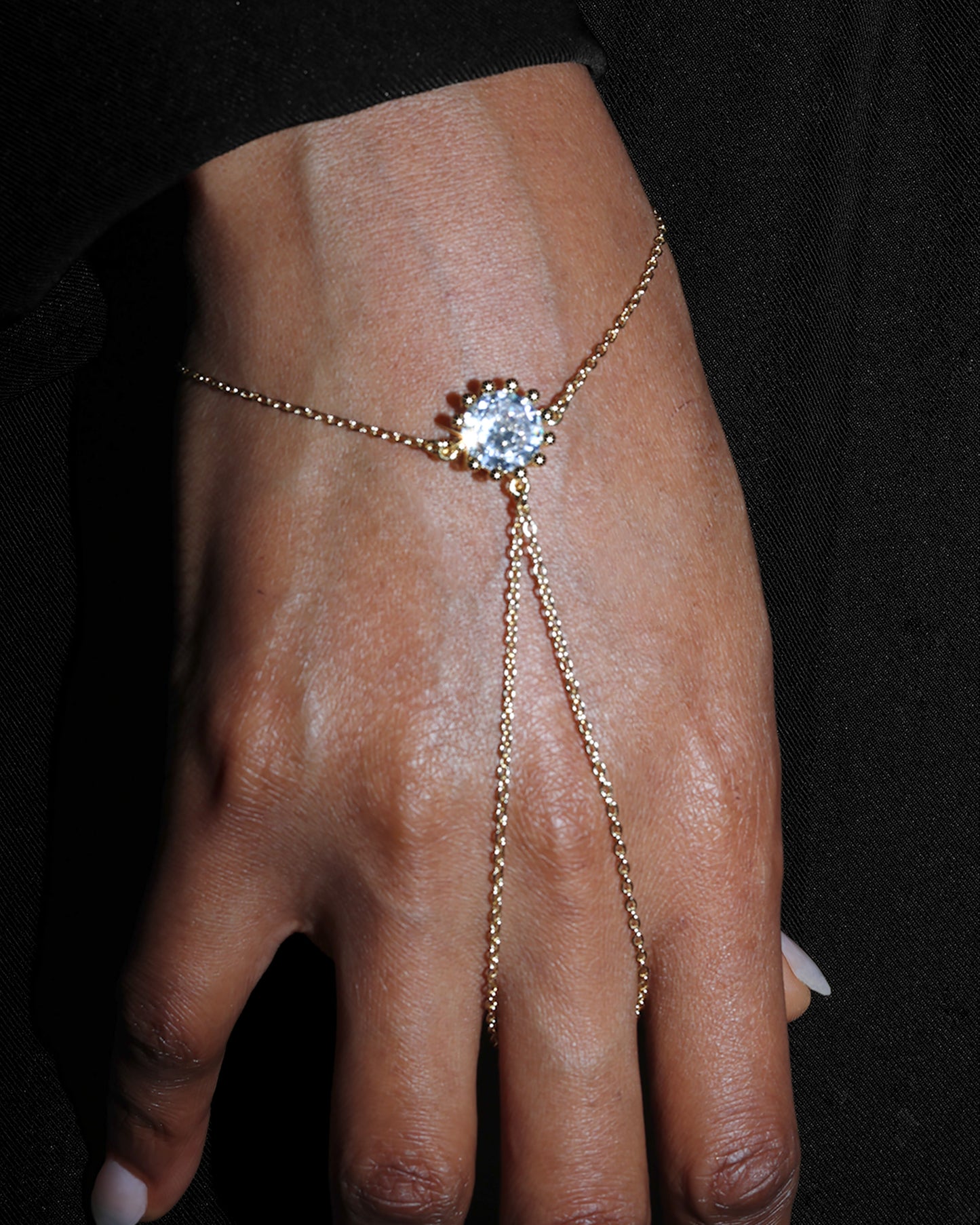 Gold hand chain with a central gemstone on a dark background