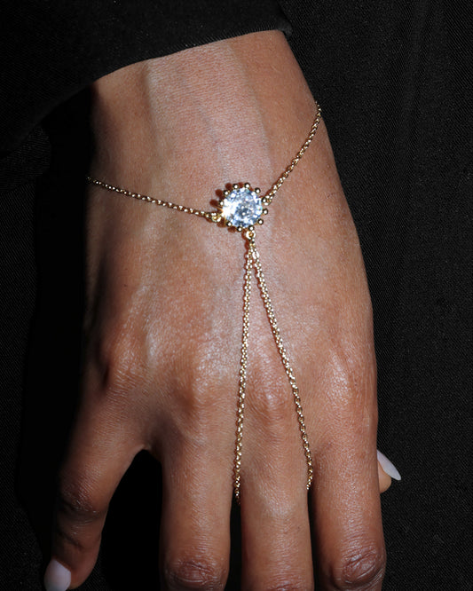 Gold hand chain with a central gemstone on a dark background