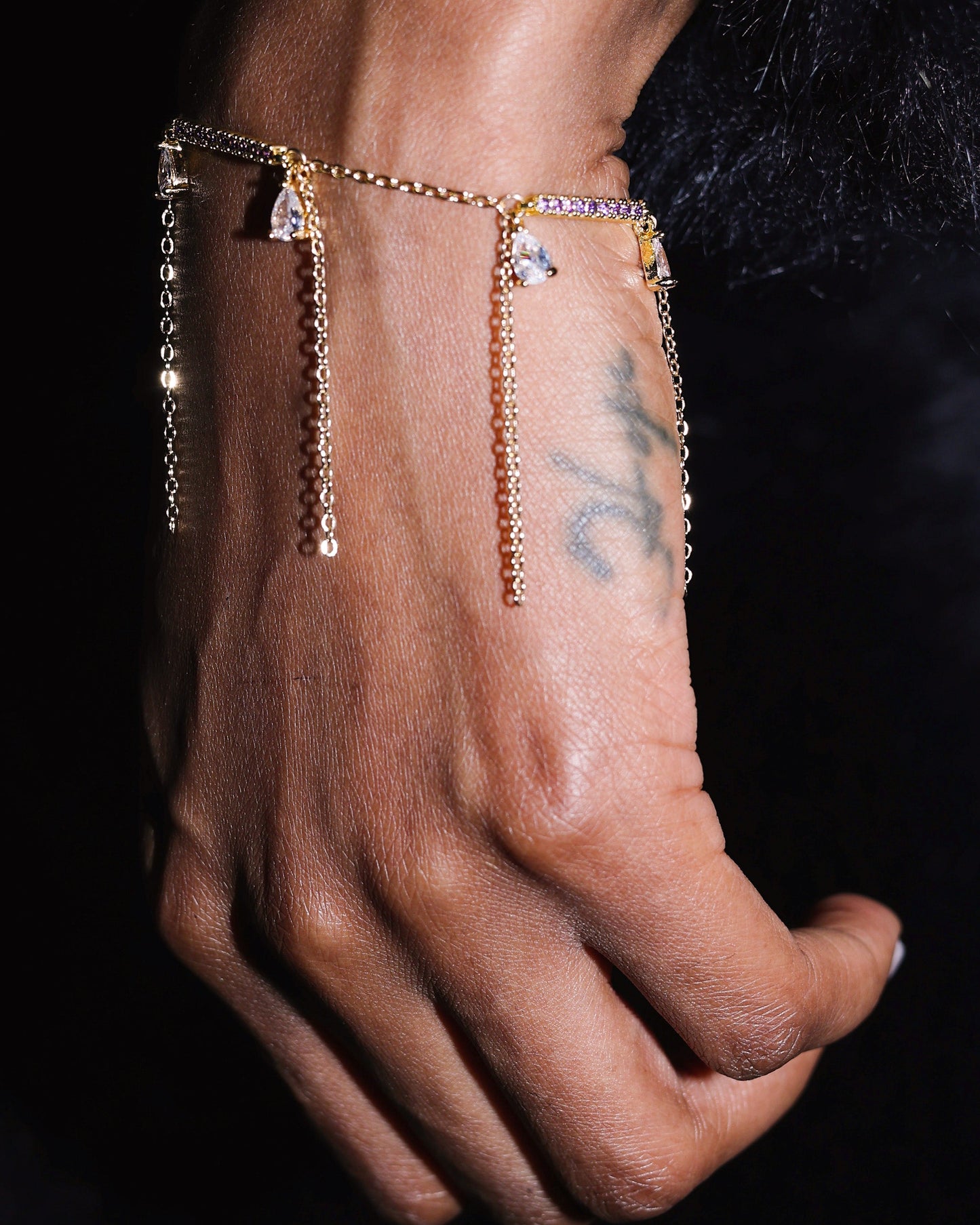 Hand wearing a gold bracelet with gemstones against a dark background