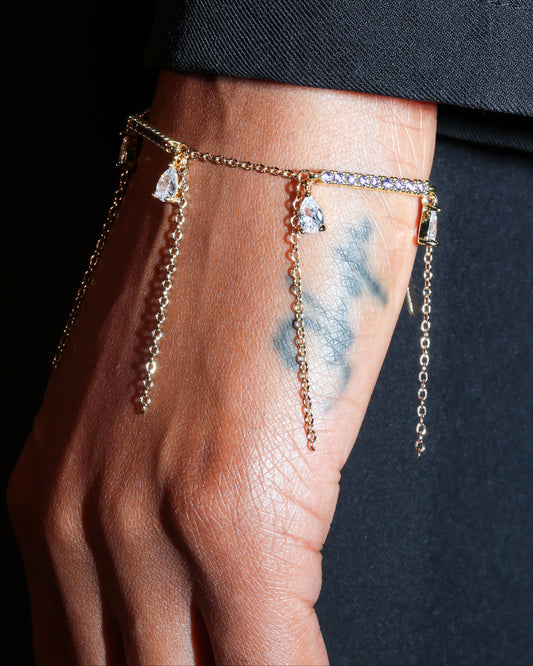 Hand wearing a delicate bracelet with small charms against a dark background