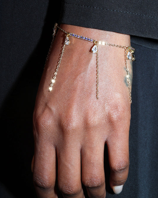 Gold chain bracelet with small stones on a person's wrist against a dark background