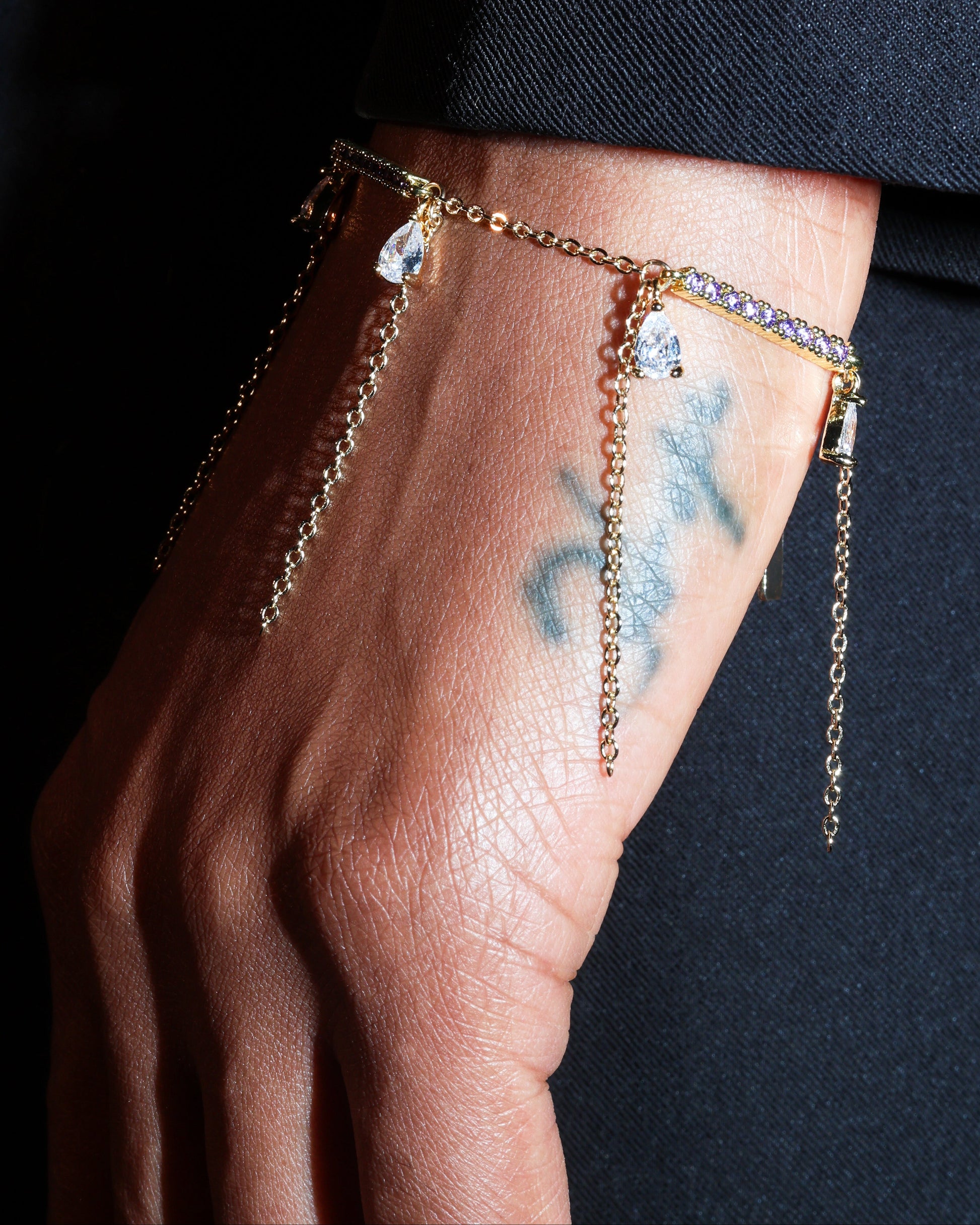 Gold chain bracelet on a wrist with a dark background