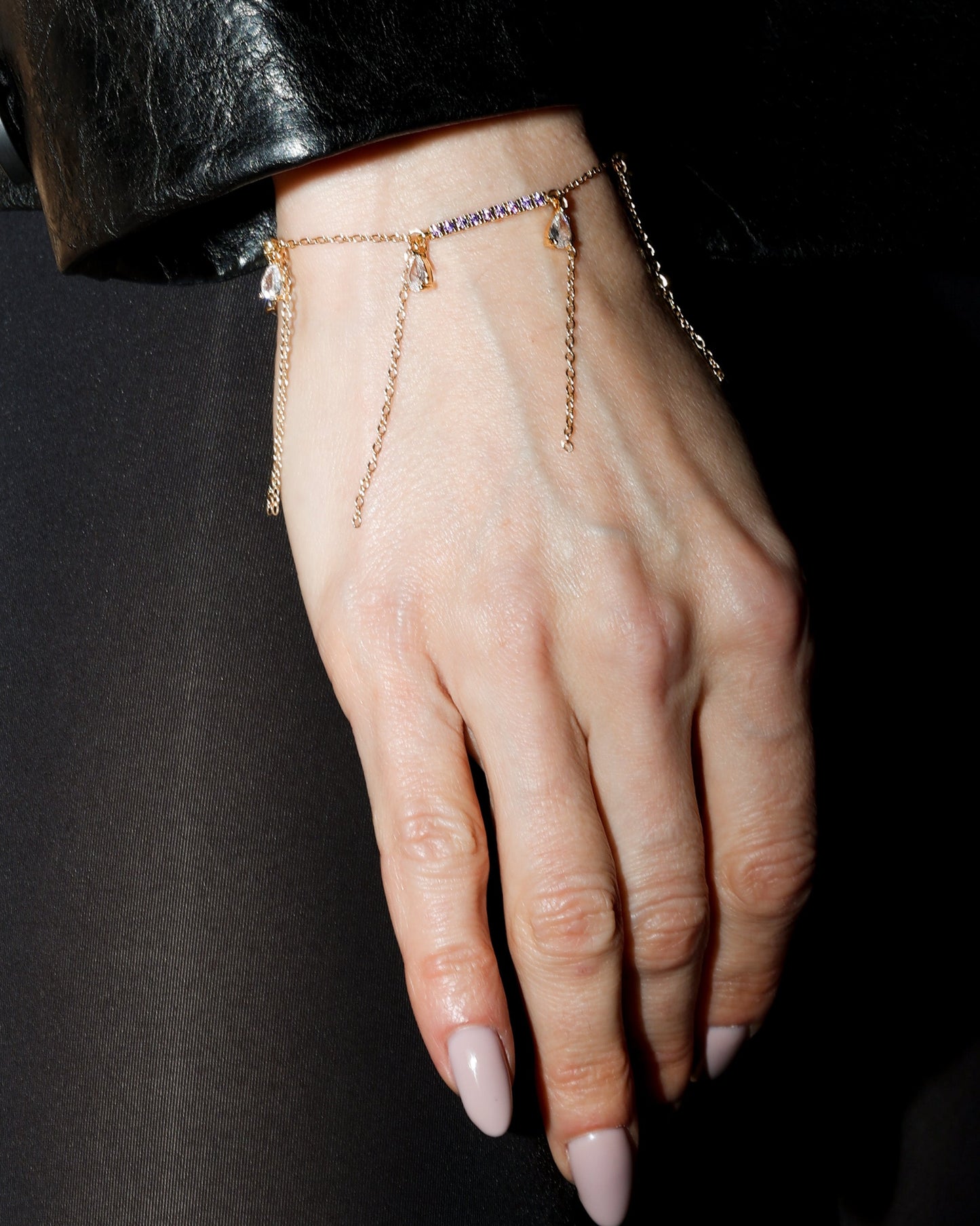 Hand wearing a delicate bracelet with a dark background