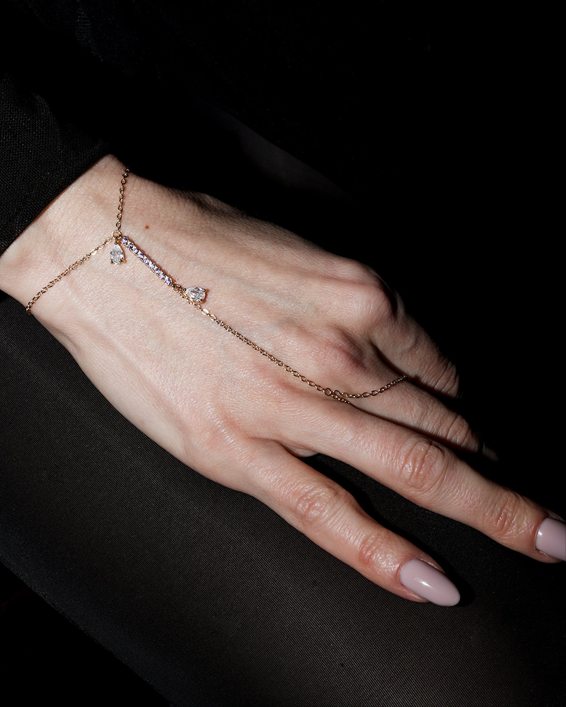 Hand wearing a delicate gold bracelet with small stones against a dark background