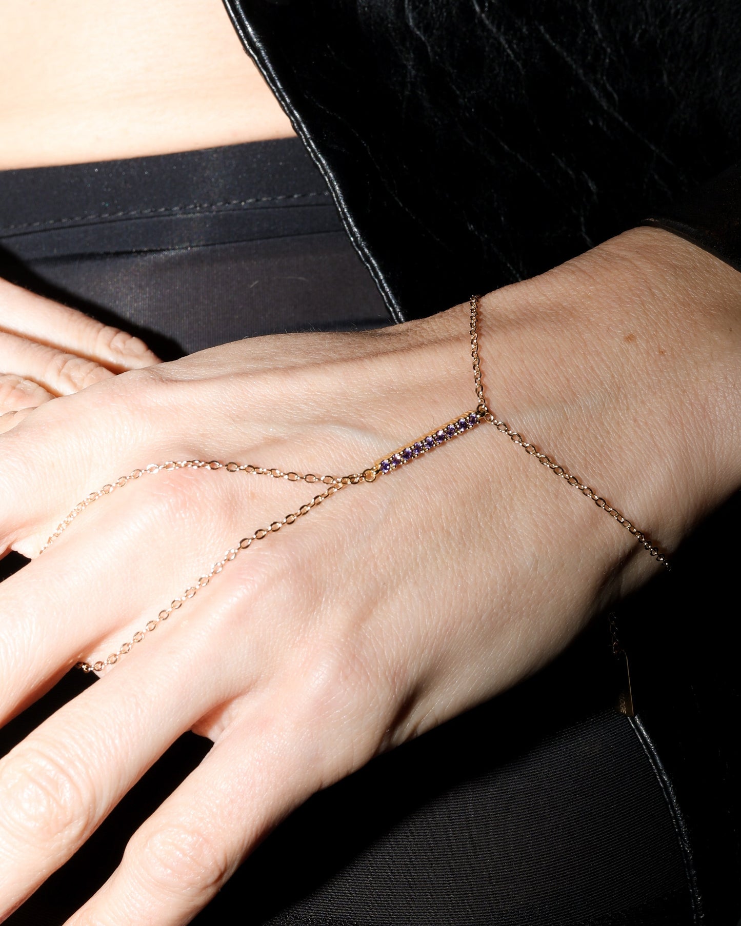 Hand wearing a delicate gold chain bracelet on a black background