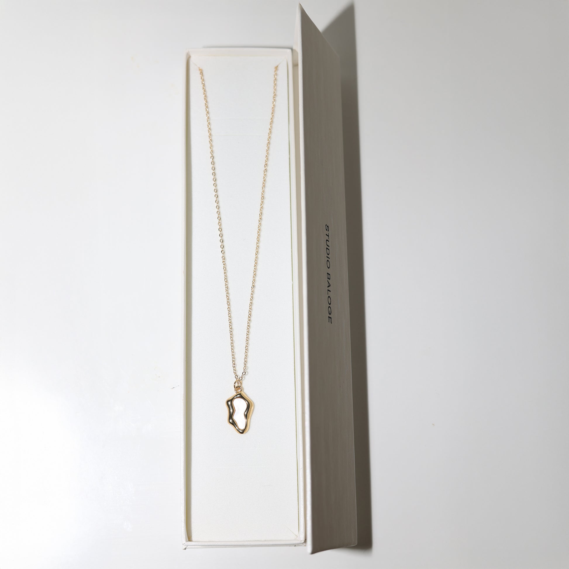 Gold necklace with a unique pendant in Studio Baloge open jewelry box on a white background