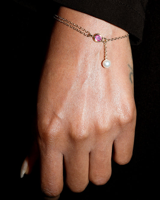 Hand wearing a delicate bracelet with a pink gemstone on a black background
