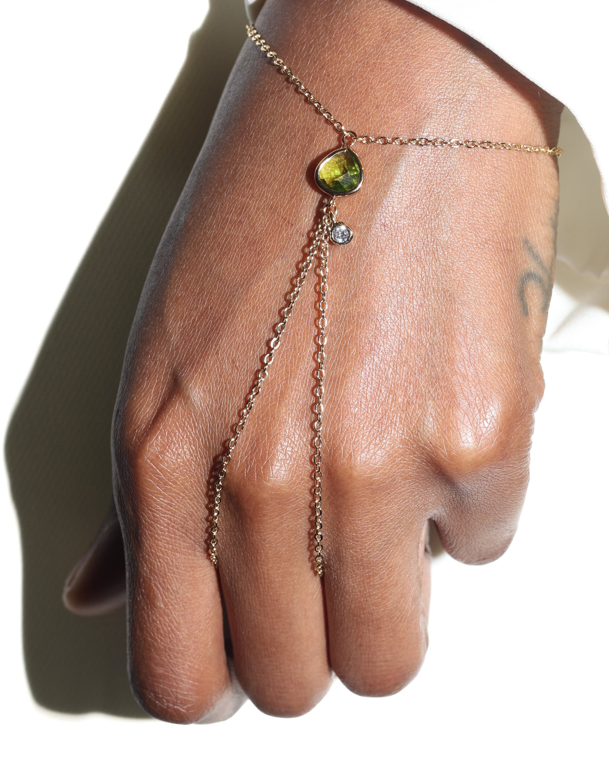 Hand wearing a delicate bracelet with a green gemstone on a neutral background