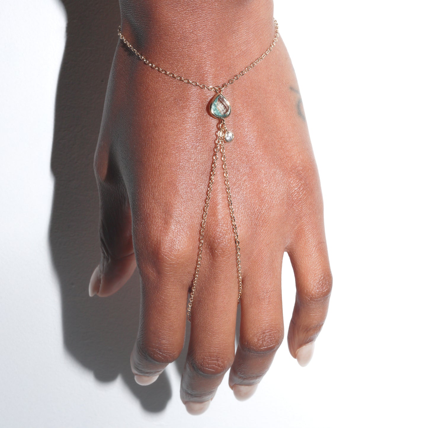 Hand wearing a delicate gold bracelet with a gemstone on a white background