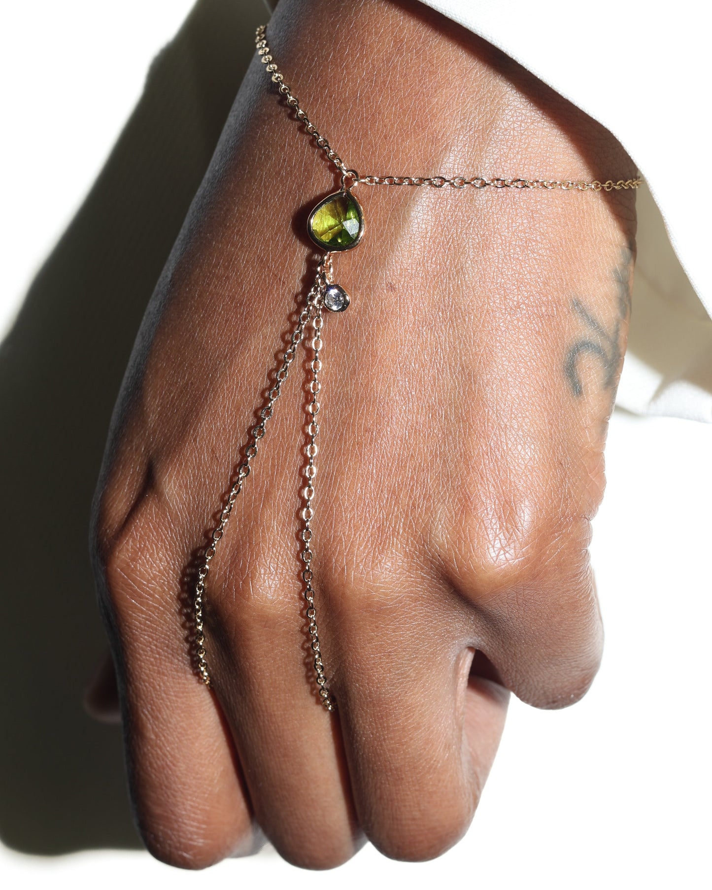 Hand wearing a delicate chain bracelet with a green gemstone on a neutral background