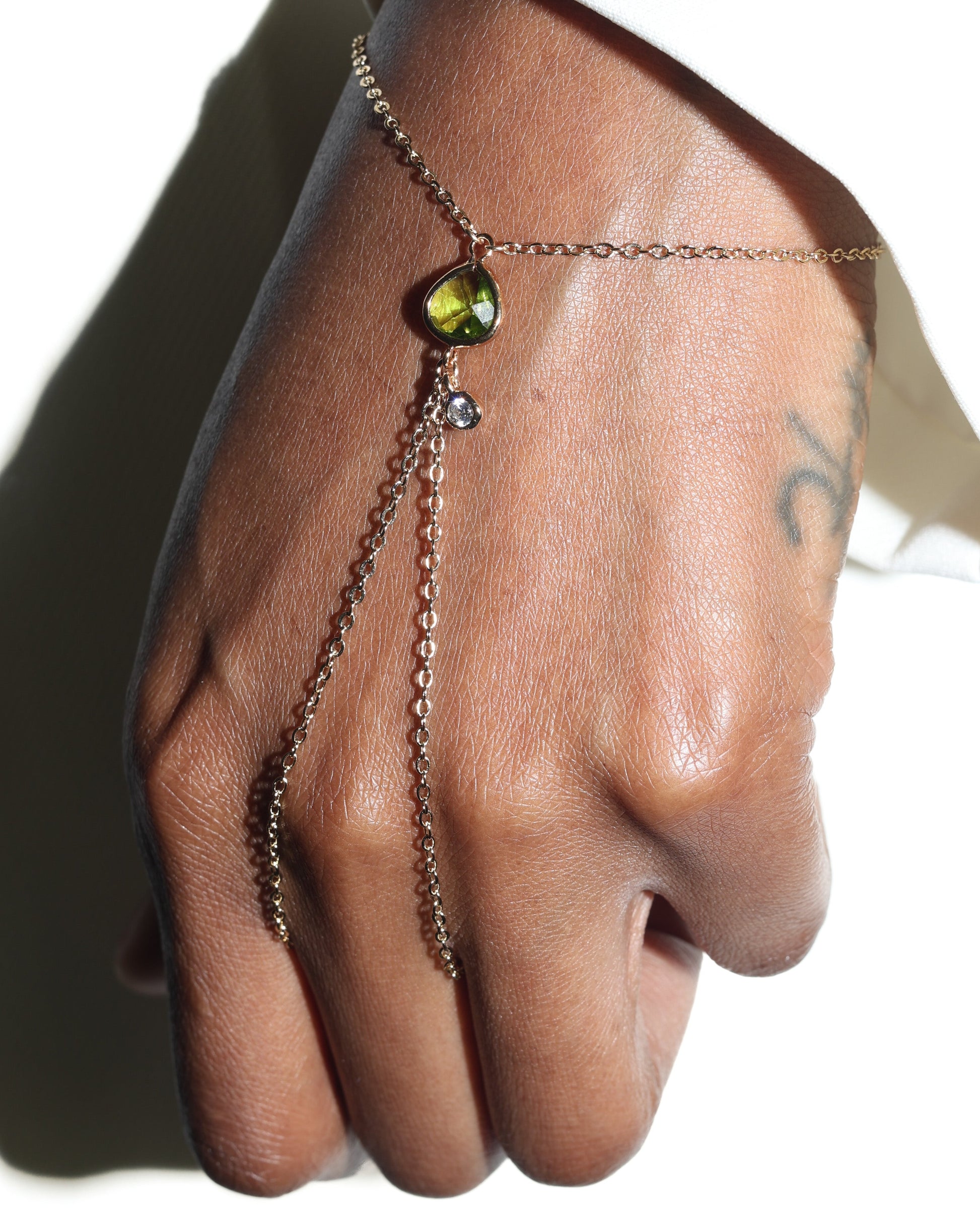 Hand wearing a delicate chain bracelet with a green gemstone on a neutral background