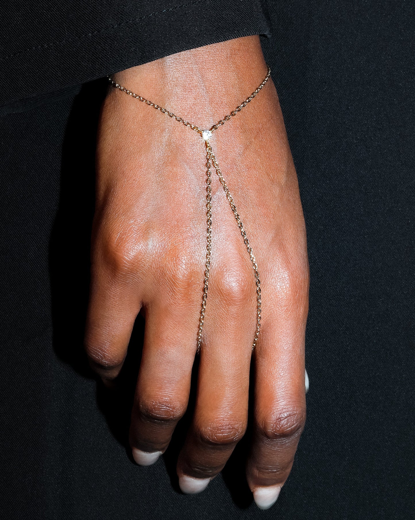 Hand wearing a delicate chain bracelet against a black background