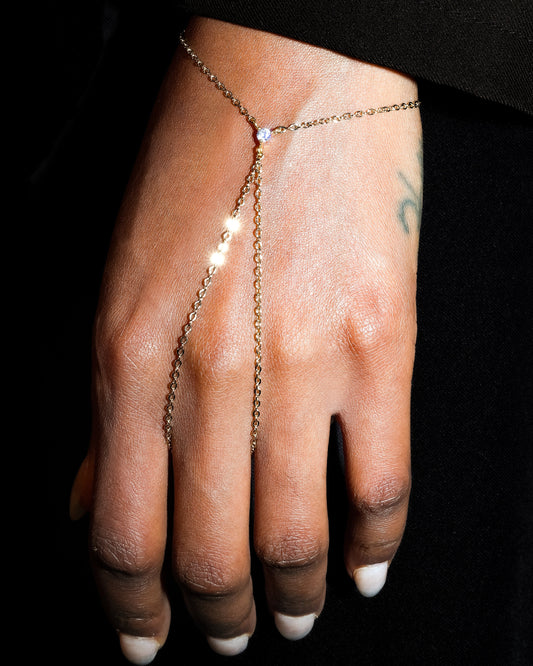 Hand wearing a delicate gold chain bracelet on a black background