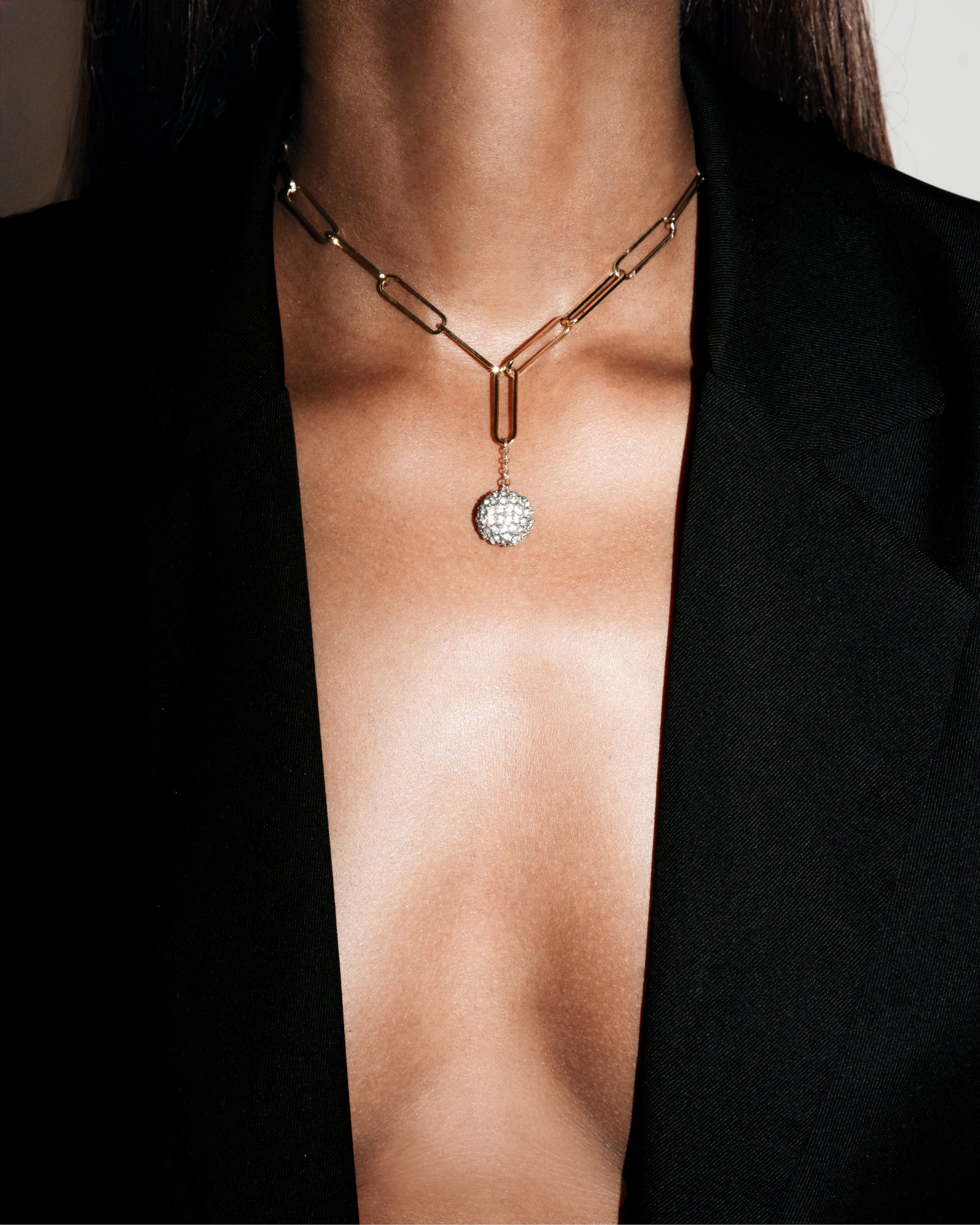 Gold necklace with a diamond pendant on a person wearing a black blazer.