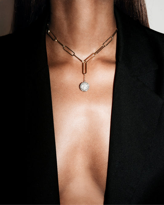 Gold necklace with a diamond pendant on a person wearing a black blazer.
