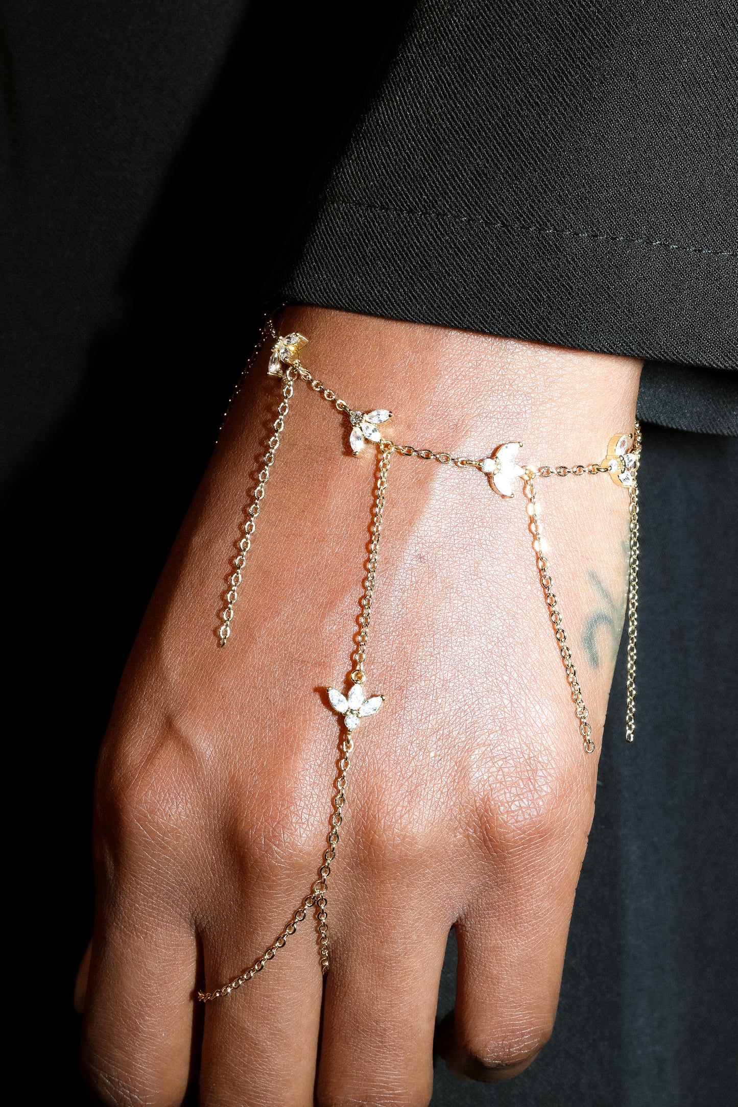 Gold chain bracelet with charms on a hand against a black background