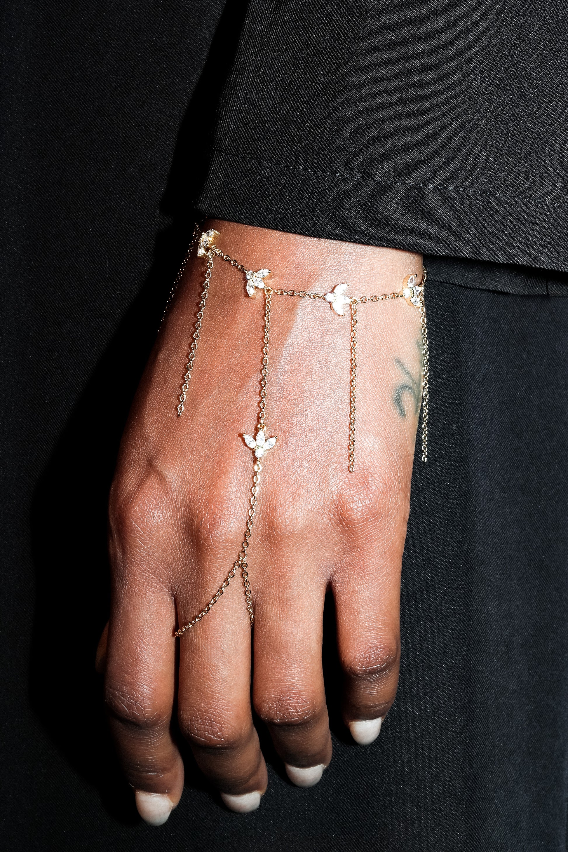 Hand wearing a delicate gold chain bracelet with small floral charms against a black background