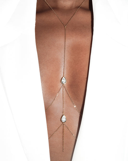 Person wearing a white blazer with a double diamond teardrop gold body chain