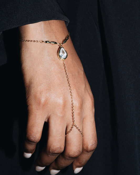Gold hand harness bracelet with a teardrop-shaped pendant on a person's wrist against a black outfit |Studio Baloge