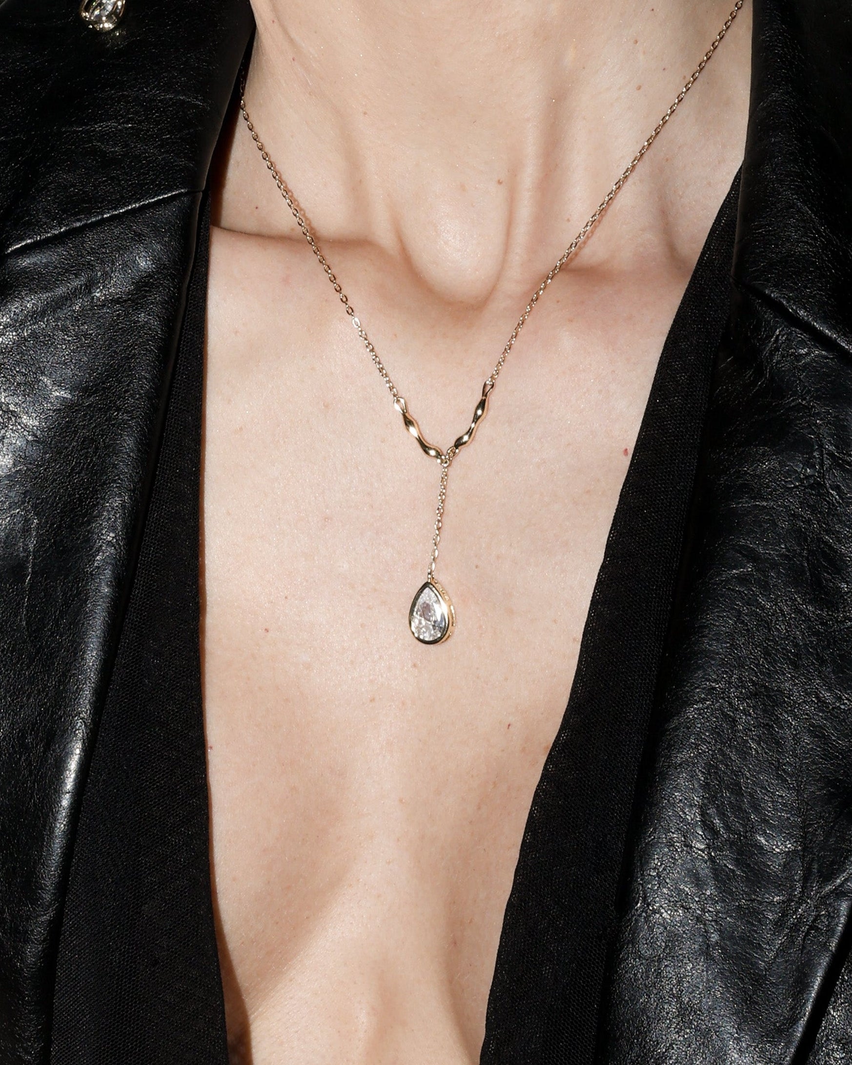 Woman wearing a black leather jacket with a deep neckline, gold  pear cut jewelry, and earrings.