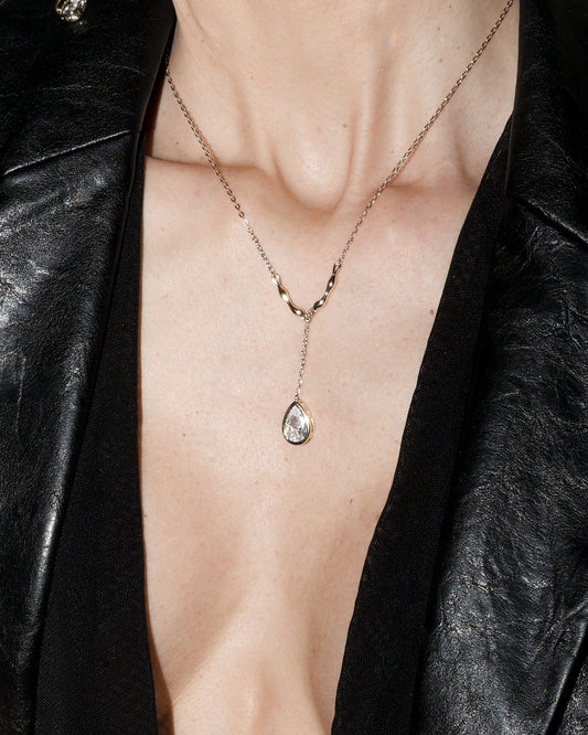 Woman wearing a black leather jacket with a deep neckline, gold  pear cut jewelry, and earrings.