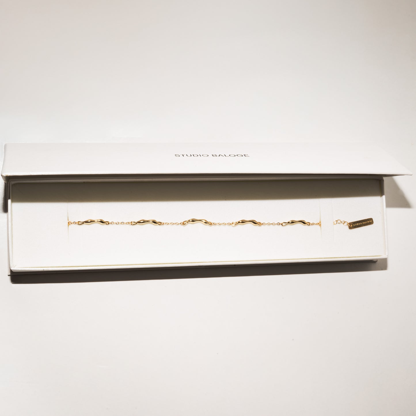 Gold bracelet in white box with 'STUDIO BALOGE' branding on a light gray background