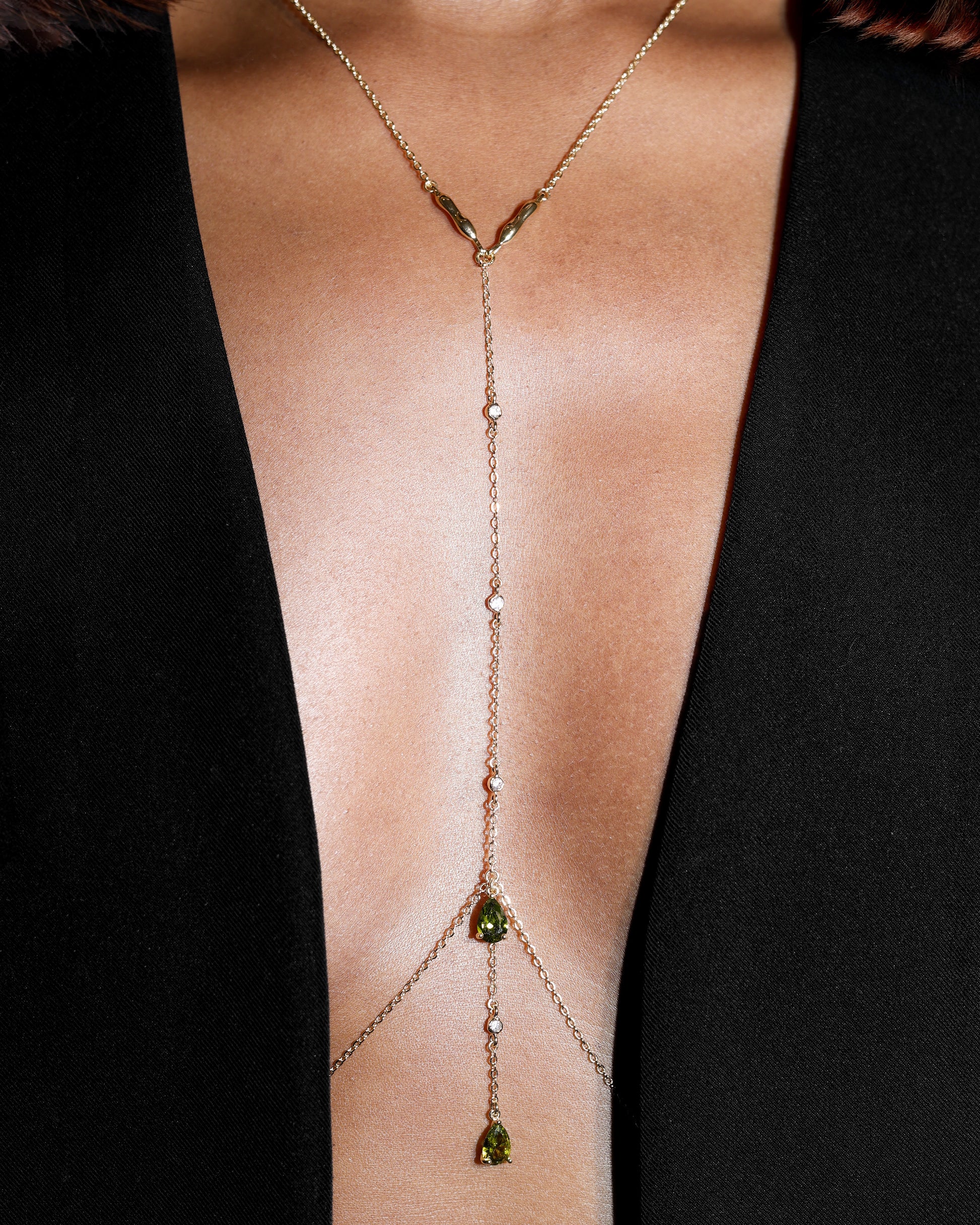Gold body chain with olive green gemstones on a black background
