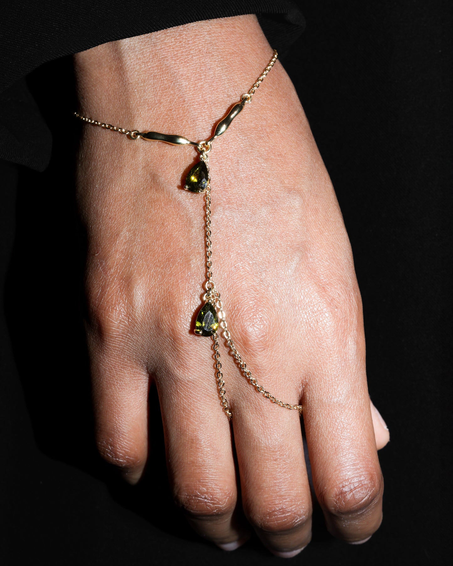 Hand wearing a delicate gold bracelet with  olive green gemstones against a dark background