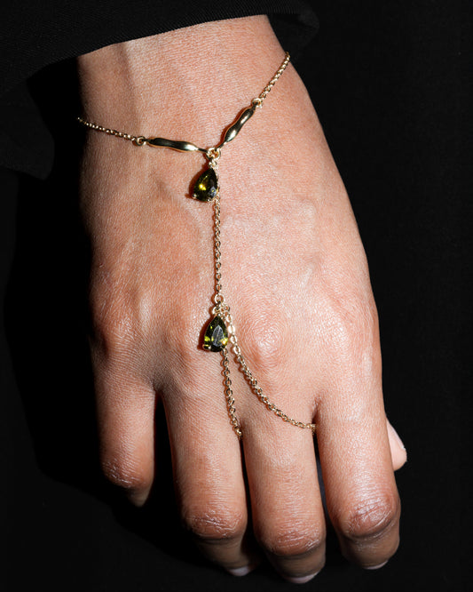 Hand wearing a delicate gold bracelet with  olive green gemstones against a dark background