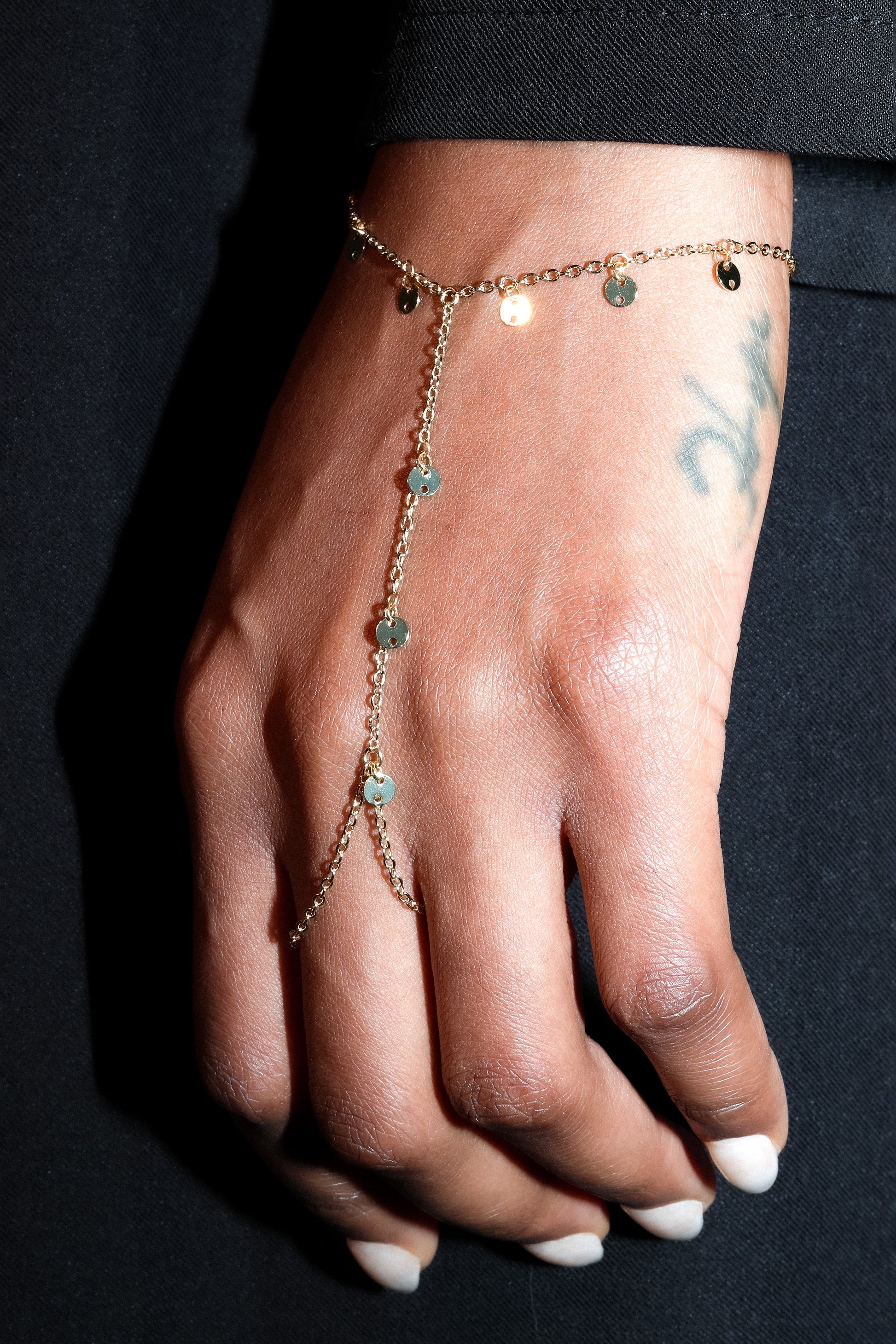 Gold delicate hand harness with fine chain and small bead details worn on hand against black fabric background