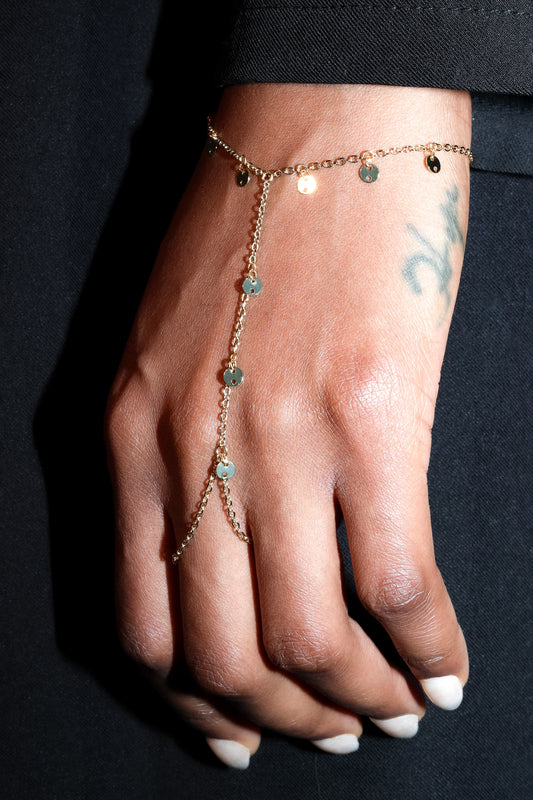 Gold delicate hand harness with fine chain and small bead details worn on hand against black fabric background