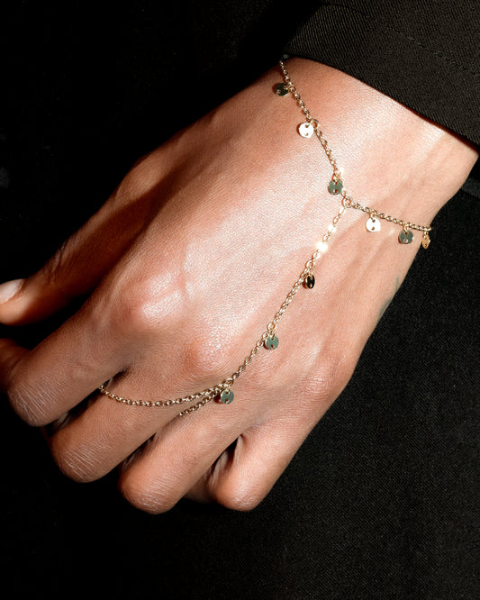 Close-up of a hand wearing a delicate hand chain bracelet on a dark background