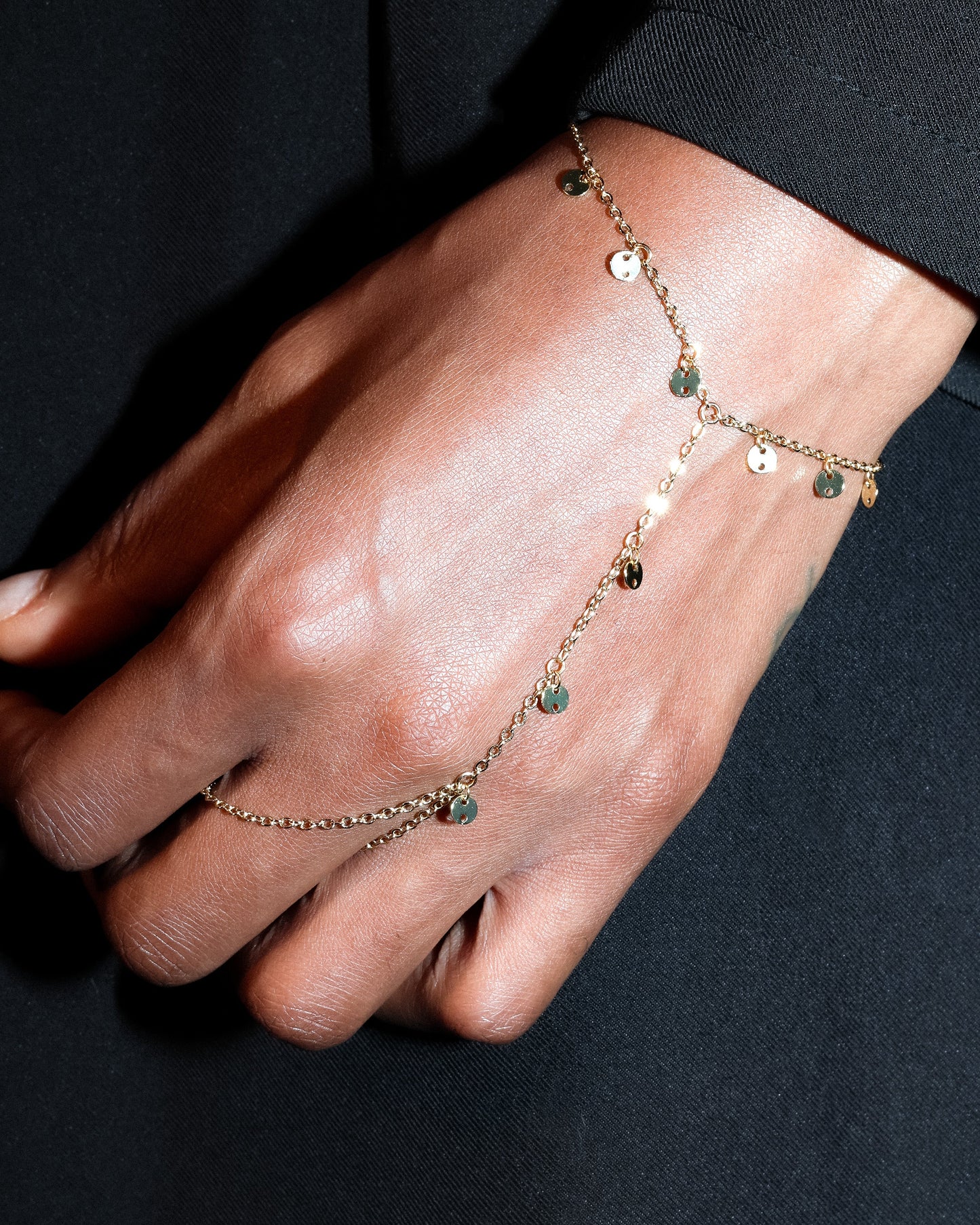 Close-up of a hand wearing a delicate hand chain bracelet on a dark background