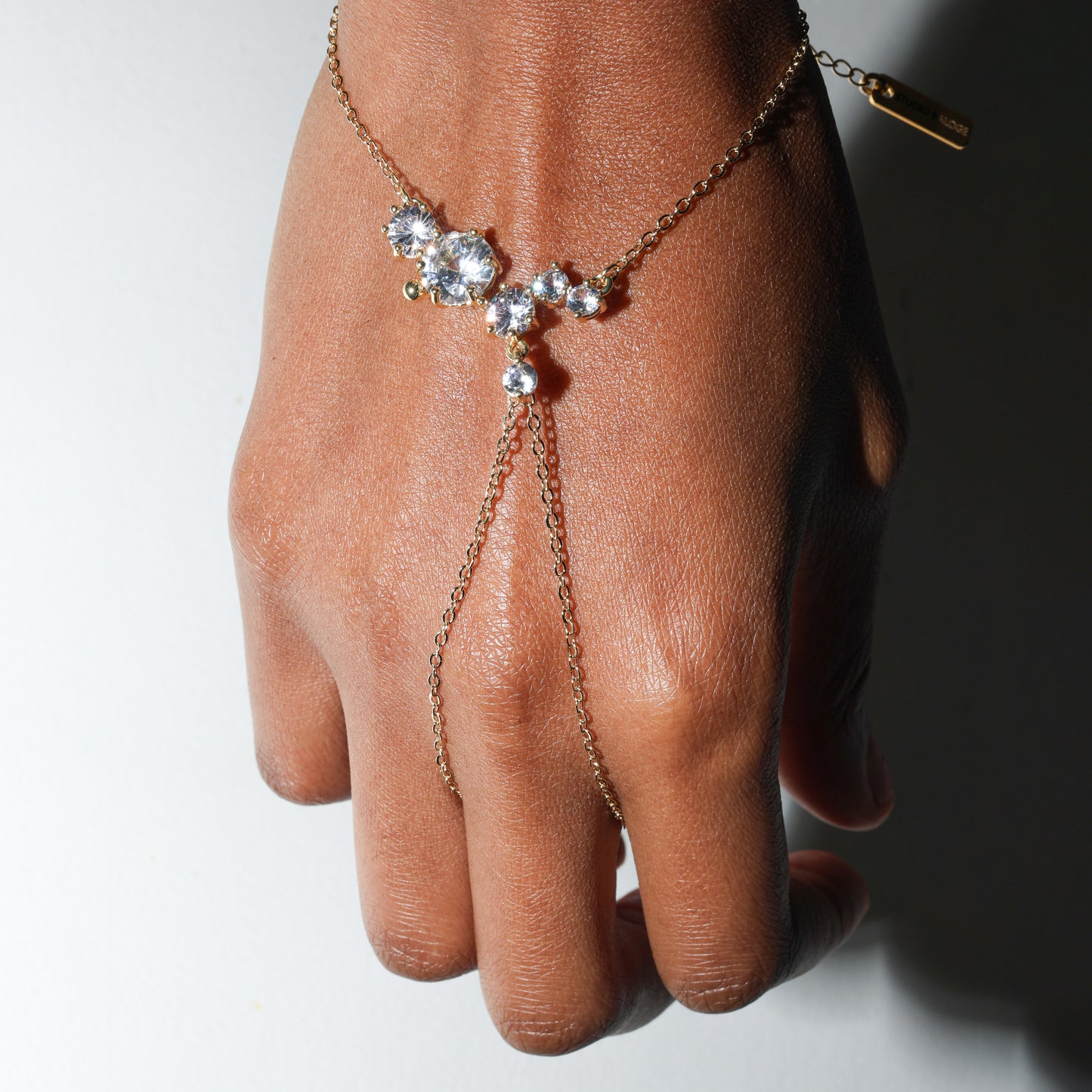 Hand wearing a delicate gold bracelet with small stones on a neutral background